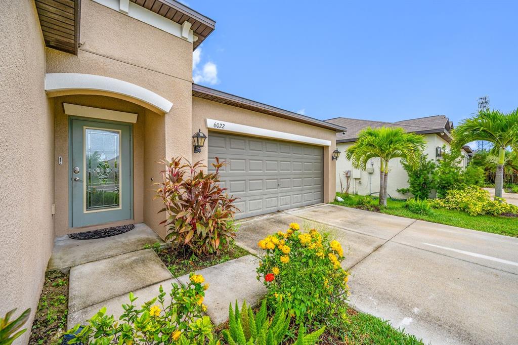 A beige house exterior features a light blue front door and a two-car garage — 6022 TREMEZA PLACE, PALMETTO, FL