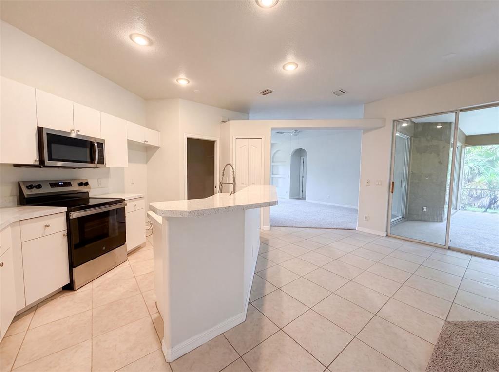 A kitchen with white cabinets, stainless steel appliances, and a breakfast bar overlooks a living area — 1796 NORA LANE, NORTH PORT, FL