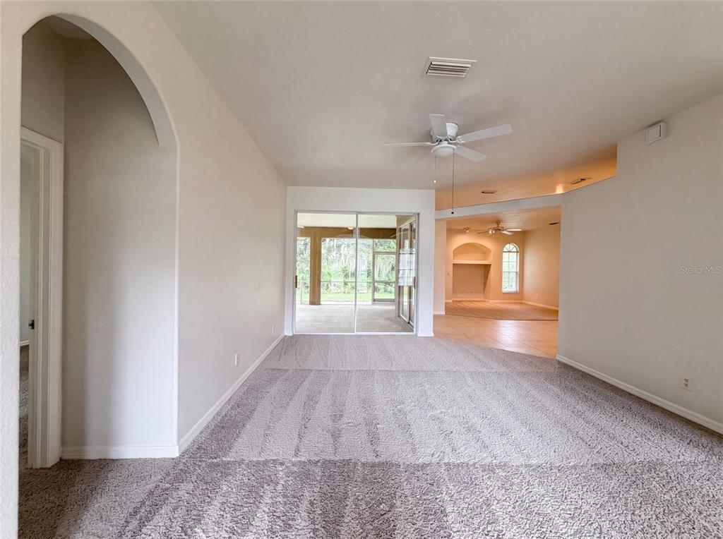 A living room with gray carpet, an arched entryway, and sliding glass doors to a patio — 1796 NORA LANE, NORTH PORT, FL