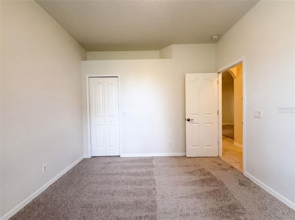 An empty bedroom features beige carpet, white walls, a closet, and an open doorway — 1796 NORA LANE, NORTH PORT, FL