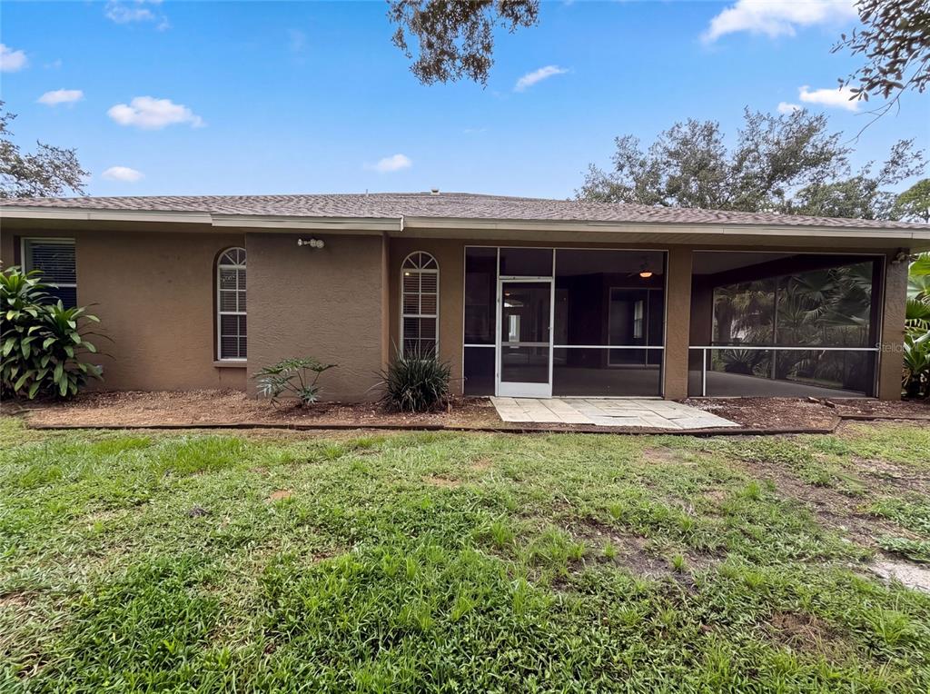 The rear exterior of a house features a screened-in porch and a grassy yard — 1796 NORA LANE, NORTH PORT, FL