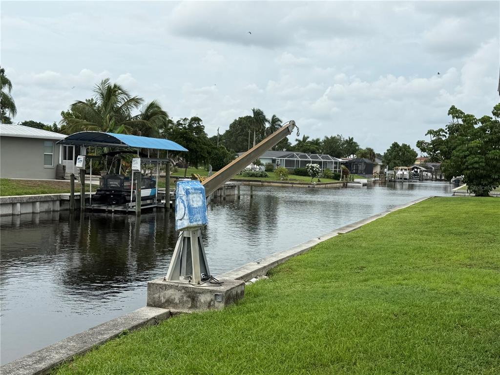 A boat lift crane stands on a concrete seawall next to a canal and lawn — 4339 S BAY CIRCLE, NORTH FORT MYERS, FL