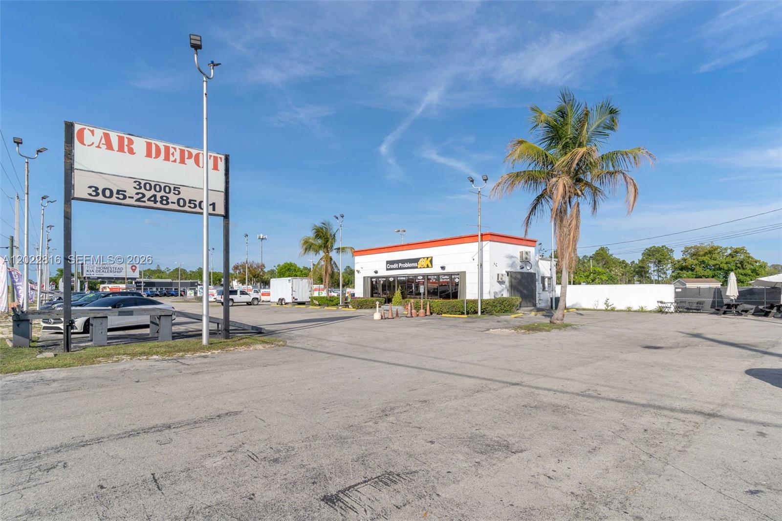 A car dealership lot features a white building, a large signage pole, and a palm tree — 30005 S Dixie Highway, Homestead FL 33033, HOMESTEAD, FL