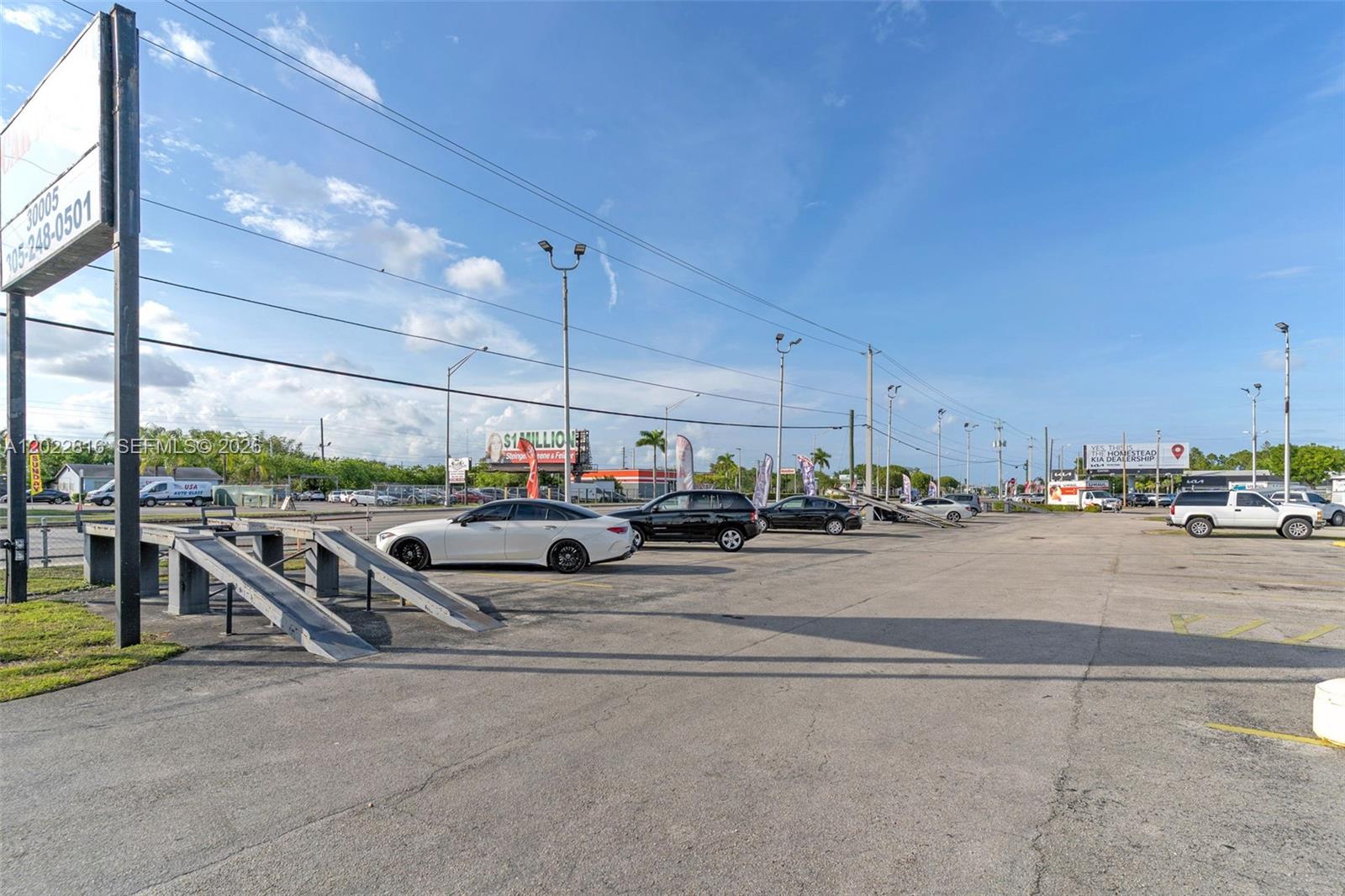 An outdoor car dealership lot features several parked vehicles and metal display ramps — 30005 S Dixie Highway, Homestead FL 33033, HOMESTEAD, FL
