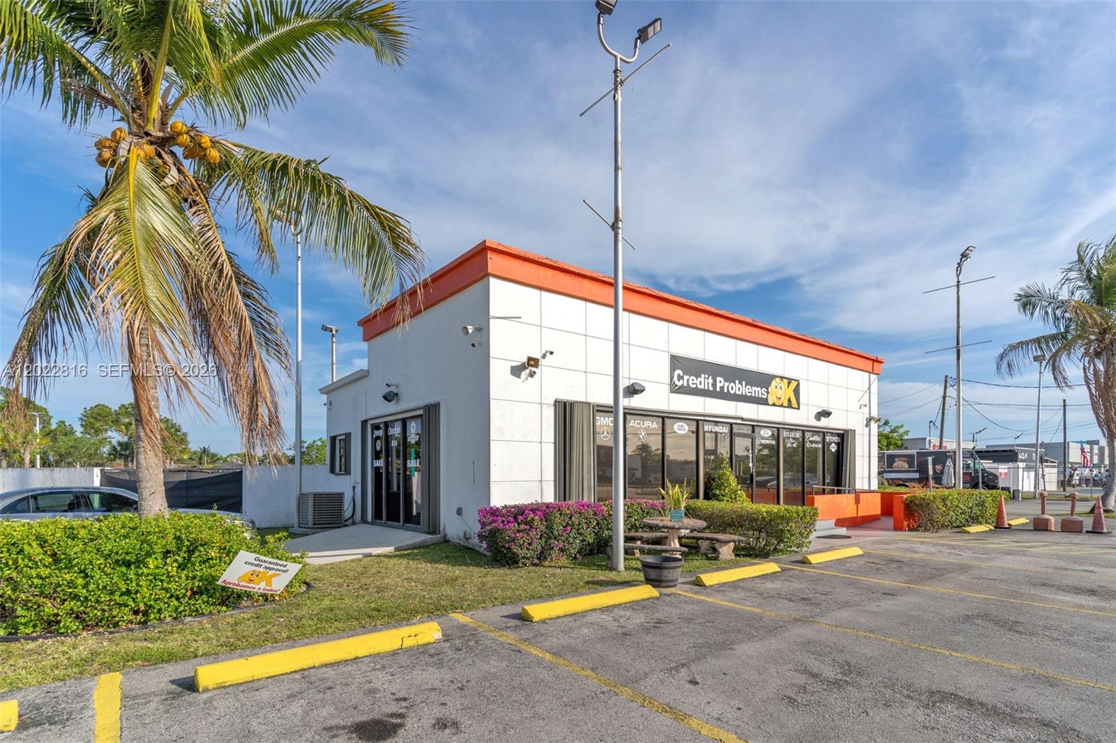 A white commercial building with an orange roof trim sits in a paved parking lot — 30005 S Dixie Highway, Homestead FL 33033, HOMESTEAD, FL