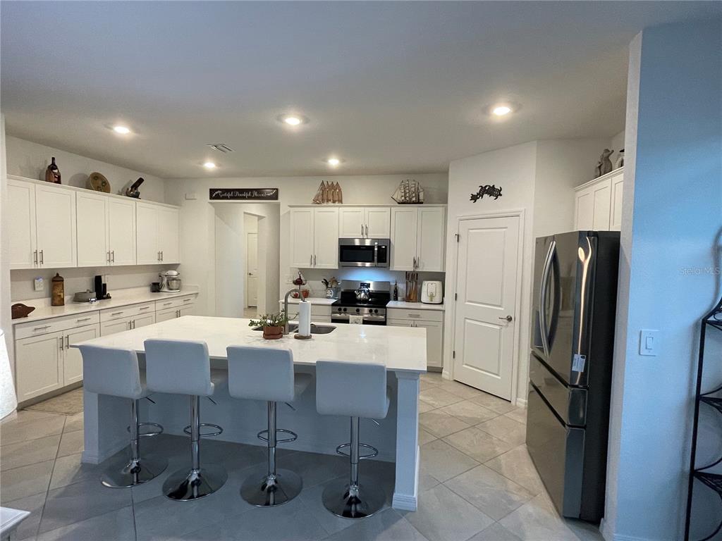 A kitchen features white cabinetry, a large central island with bar seating, and stainless appliances — 11321 PINOT DRIVE, VENICE, FL