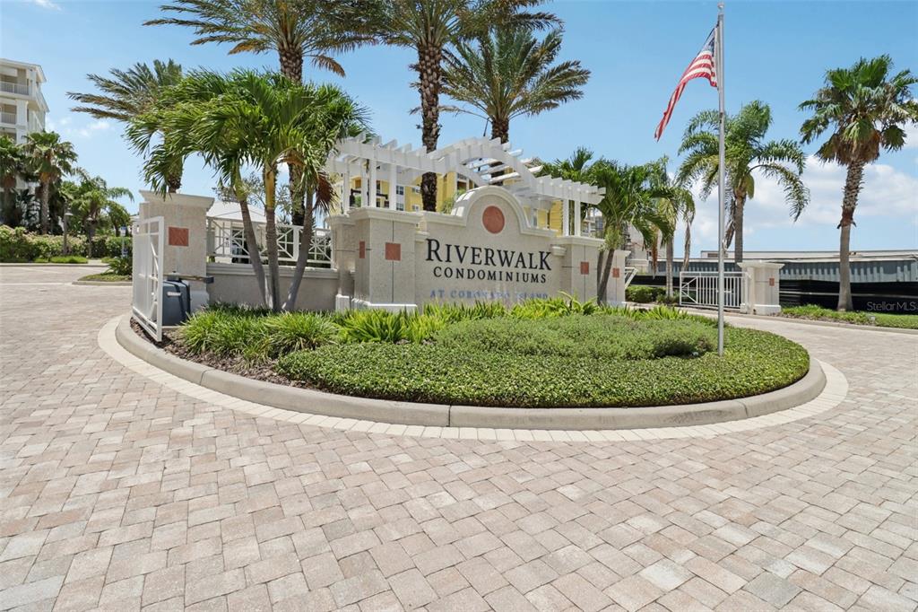 The entrance to Riverwalk Condominiums features a stone monument sign, landscaping, and palm trees — 7 RIVERWALK DRIVE UNIT 406, NEW SMYRNA BEACH, FL