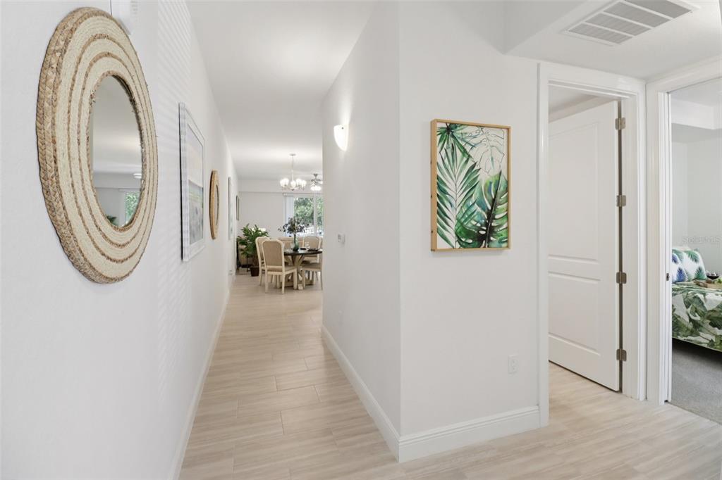 A hallway with light wood-look flooring leads to a dining area with a round table — 7 RIVERWALK DRIVE UNIT 406, NEW SMYRNA BEACH, FL