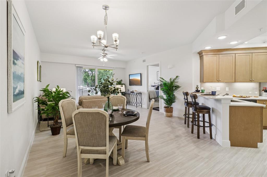 An open-concept dining and kitchen area features light wood cabinets, tile flooring, and a chandelier — 7 RIVERWALK DRIVE UNIT 406, NEW SMYRNA BEACH, FL