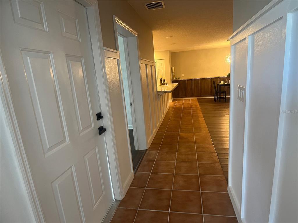 A tiled hallway leads past a white door and wainscoting toward a dining area — 2954 PEACH STREET, LEESBURG, FL