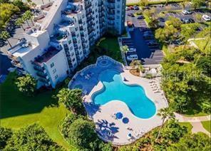 An aerial view shows a multi-story apartment building next to a large, irregularly shaped swimming pool — 6165 CARRIER DRIVE UNIT 1215, ORLANDO, FL