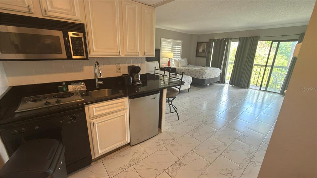 A studio apartment features a kitchen with white cabinets, black countertops, and an adjacent bedroom — 6165 CARRIER DRIVE UNIT 1215, ORLANDO, FL