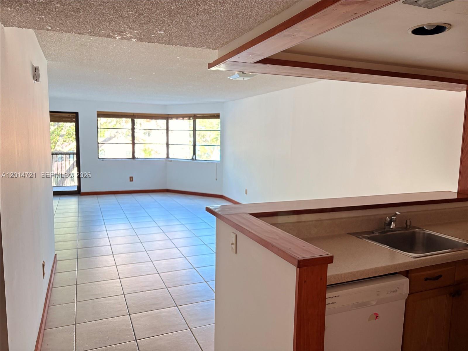 A kitchen counter overlooks an open living area with tiled floors and large windows — 20860 San Simeon Way # 6, Miami FL 33179, MIAMI, FL