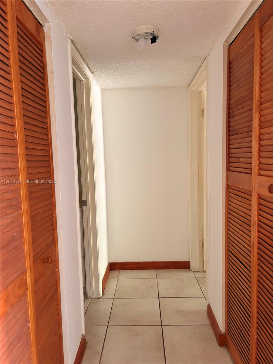 A narrow hallway features white walls, tiled flooring, and wooden louvered closet doors on both sides — 20860 San Simeon Way # 6, Miami FL 33179, MIAMI, FL