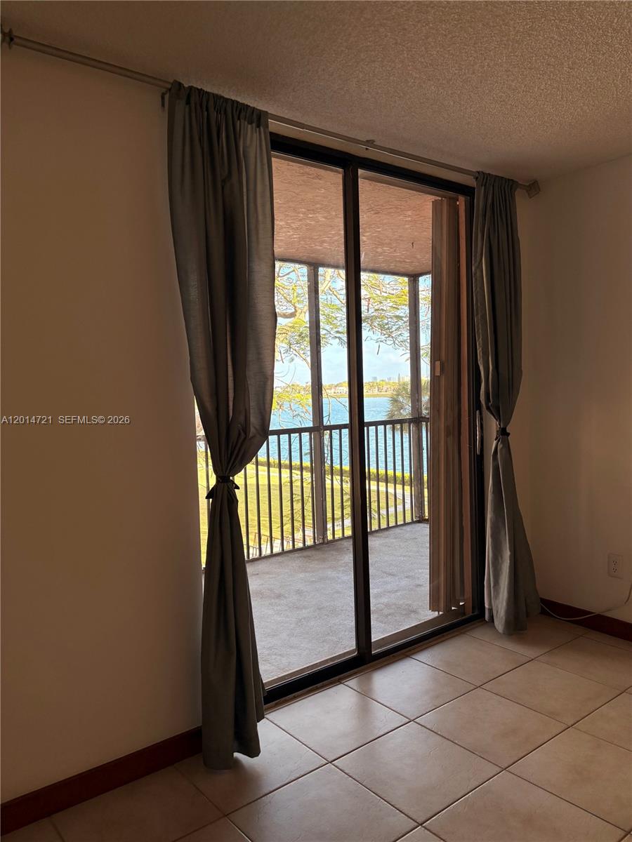 A room with tiled floors features sliding glass doors opening to a screened balcony overlooking water — 20860 San Simeon Way # 6, Miami FL 33179, MIAMI, FL