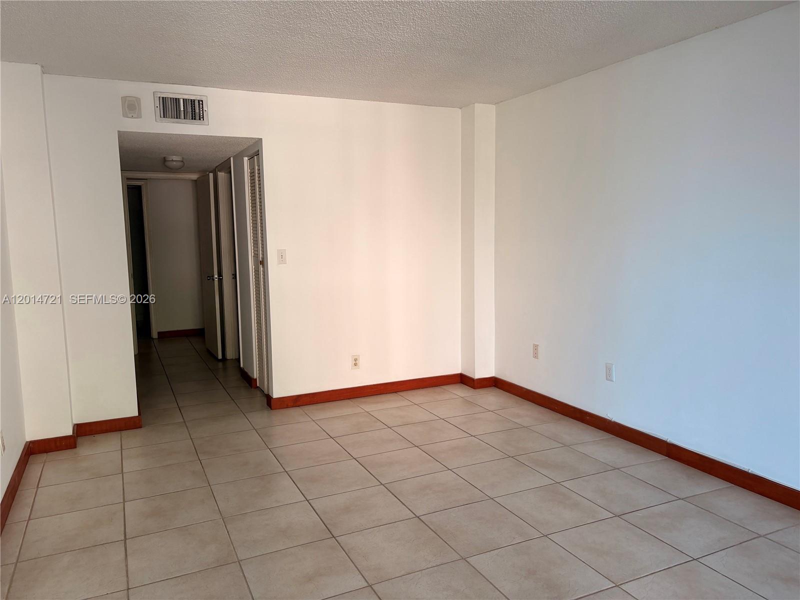An empty room features white walls, beige tile flooring, and dark wood baseboards — 20860 San Simeon Way # 6, Miami FL 33179, MIAMI, FL
