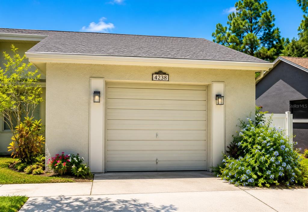 A beige one-car garage with a white door and two wall-mounted exterior lights — 4238 PINEFIELD AVENUE, HOLIDAY, FL