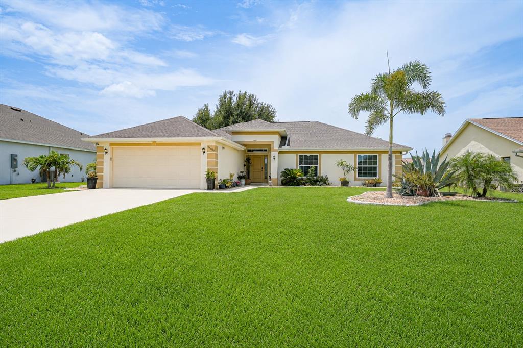 A single-story suburban house with a beige exterior, a two-car garage, and a palm tree — 26403 RAMPART BOULEVARD, PUNTA GORDA, FL