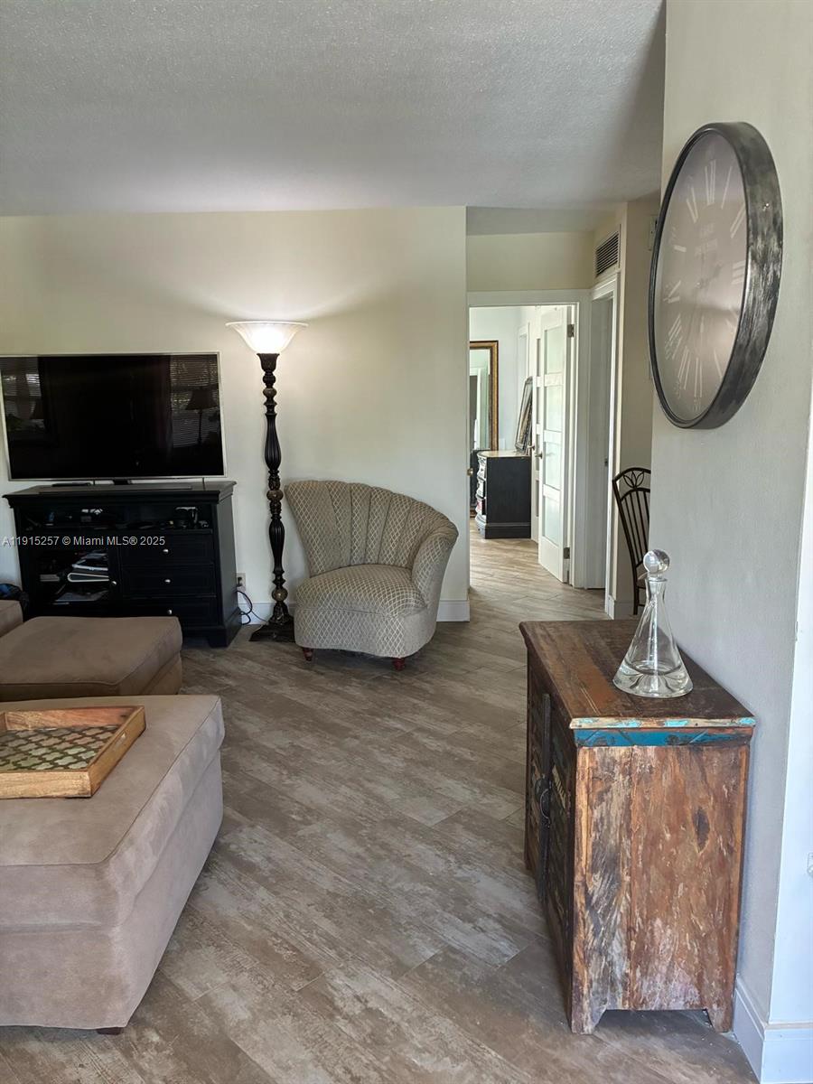 A living room features light wood-look flooring, a television console, an accent chair, and decor — 2050 NE 39th St # 311, Lighthouse Point FL 33064, LIGHTHOUSE POINT, FL