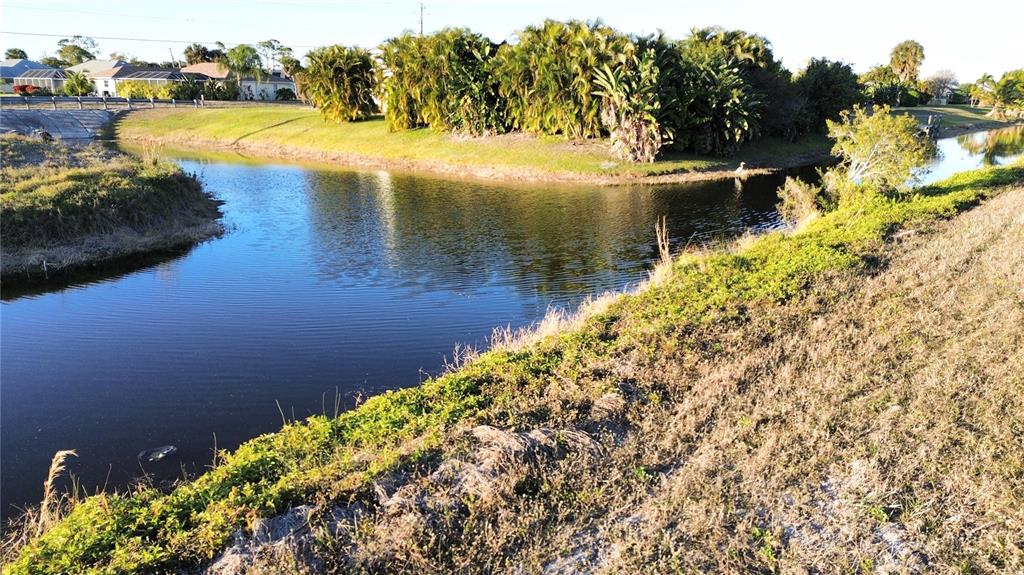 A canal flows past a grassy bank with dense tropical landscaping and nearby residential homes — 238 BROADMOOR LANE, ROTONDA WEST, FL