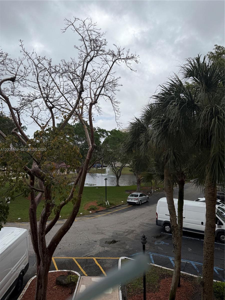 An outdoor view of a parking lot, trees, and a small pond with a fountain — 7031 Environ Blvd # 221, Lauderhill FL 33319, LAUDERHILL, FL