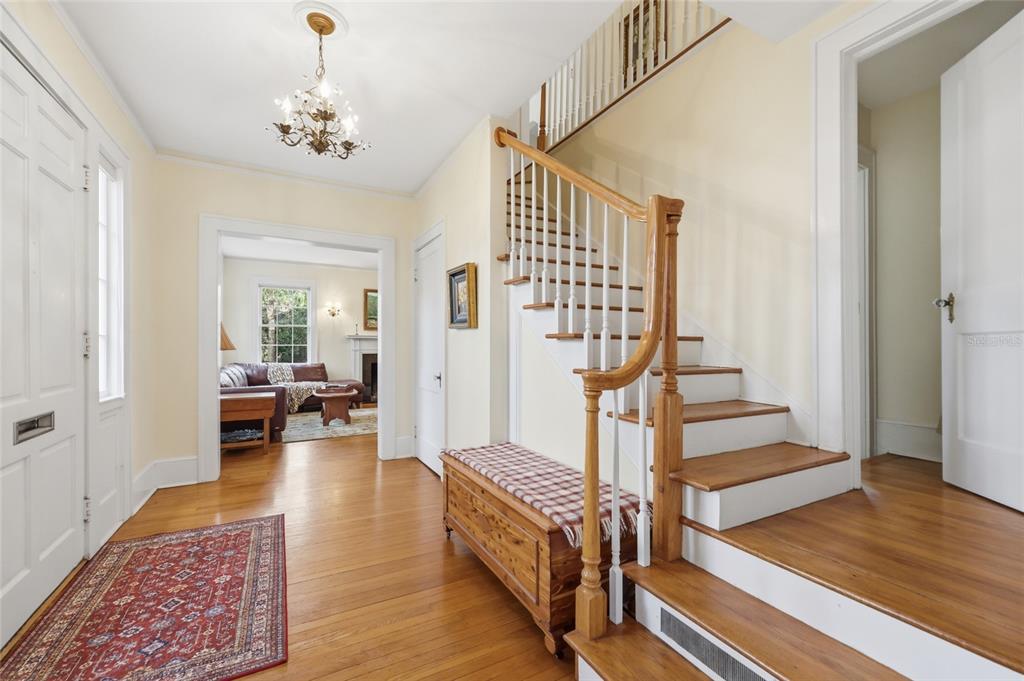 A foyer features hardwood floors, a wooden staircase with white railings, and a chandelier — 2150 NW 7TH LANE, GAINESVILLE, FL