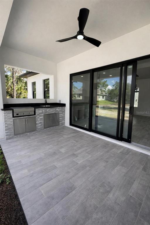 A covered patio features a built-in outdoor kitchen, gray tile flooring, and a ceiling fan — 1089 CORNELIUS BOULEVARD, PORT CHARLOTTE, FL