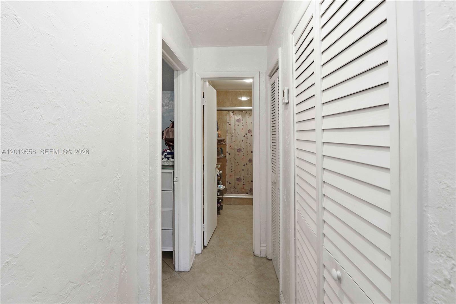 A hallway features white walls, tile flooring, and louvered closet doors leading to a bathroom — 1275 W 35th St # 45B, Hialeah FL 33012, HIALEAH, FL