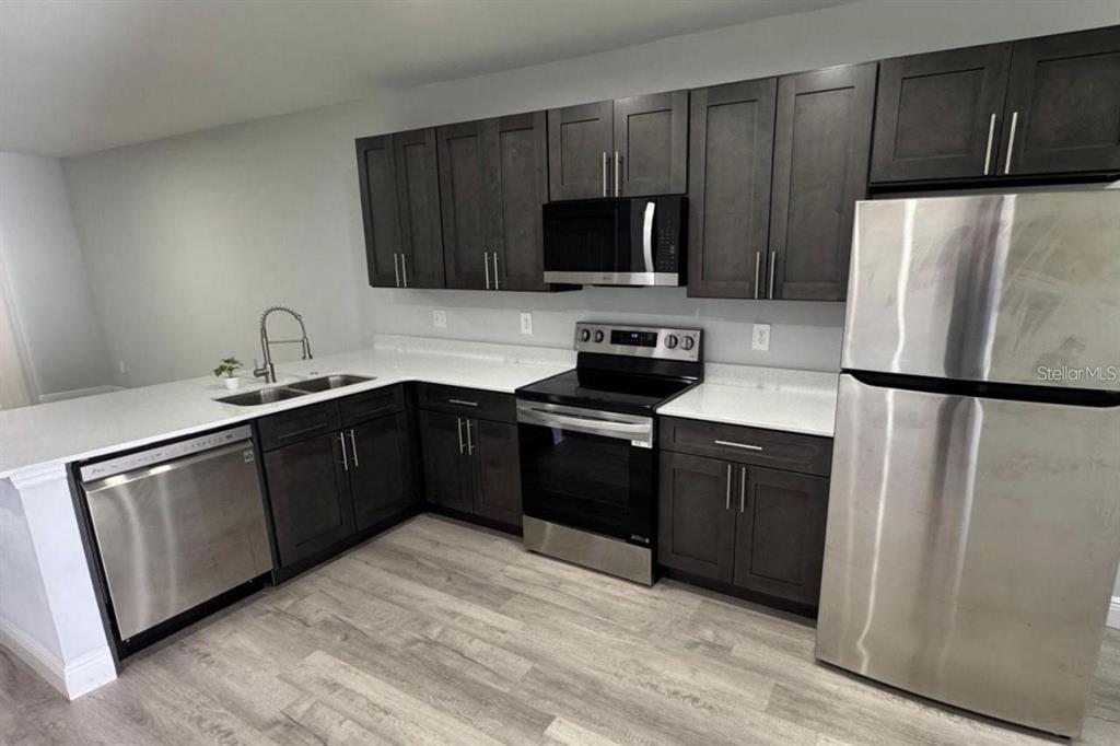 A kitchen features dark wood cabinets, stainless steel appliances, and white countertops — 985 NW 57TH COURT UNIT B, OCALA, FL