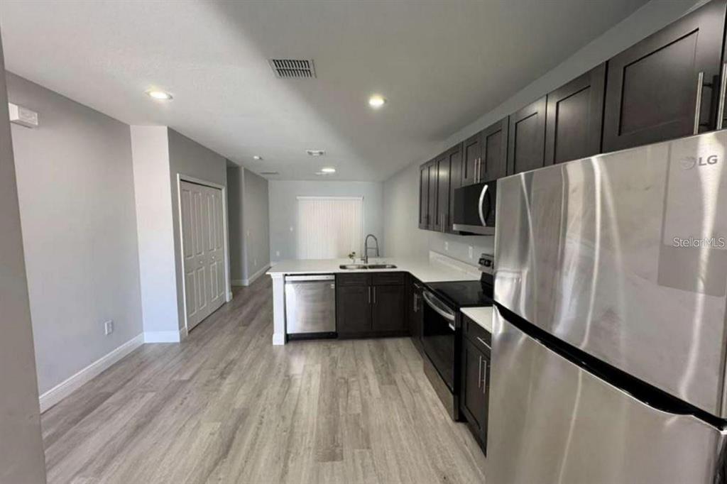 A kitchen with dark cabinets, stainless steel appliances, and light wood-look flooring — 985 NW 57TH COURT UNIT B, OCALA, FL