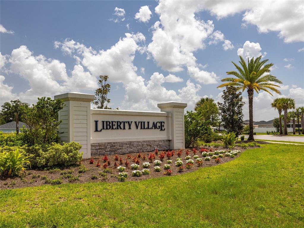 A stone and stucco monument sign for Liberty Village sits in a landscaped grassy area — 7875 SW 74TH LOOP, OCALA, FL