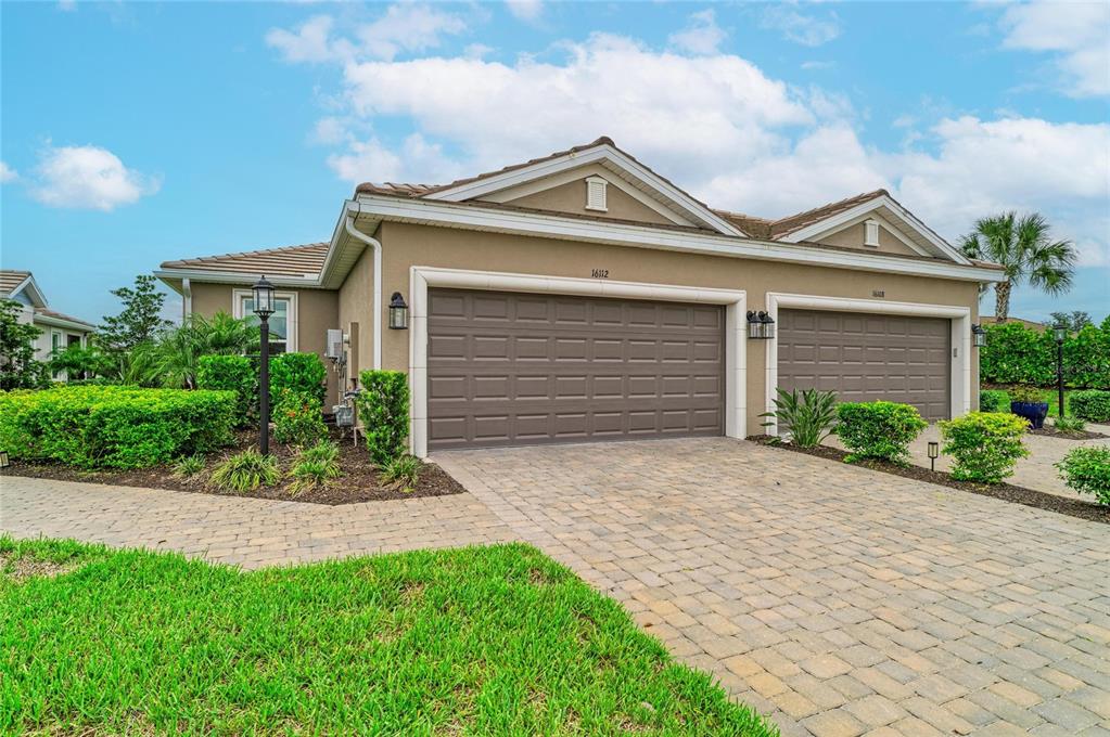 A tan house with a three-car garage and a paved driveway under a blue sky — 16112 ISOLA PLACE, BRADENTON, FL