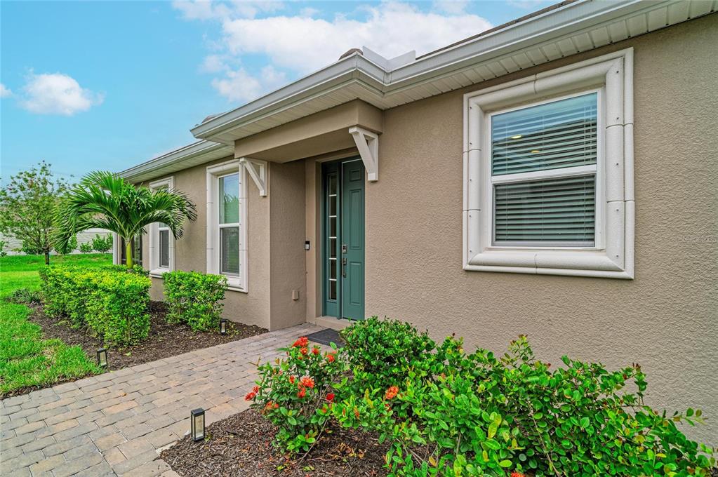 The exterior of a tan house features a front door, windows, and a landscaped walkway — 16112 ISOLA PLACE, BRADENTON, FL