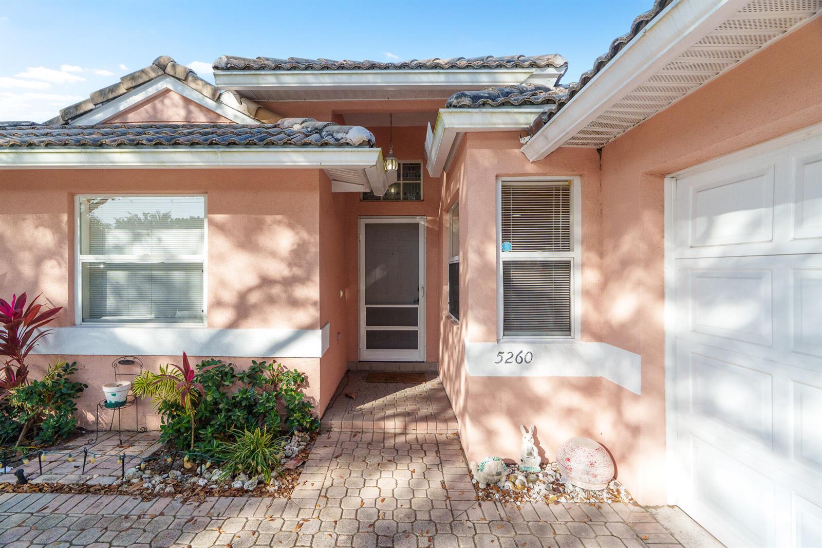 The exterior of a peach-colored house features a tiled roof, a paved walkway, and a garage — 5260 Grande Palm Circle, Delray Beach FL 33484, DELRAY BEACH, FL
