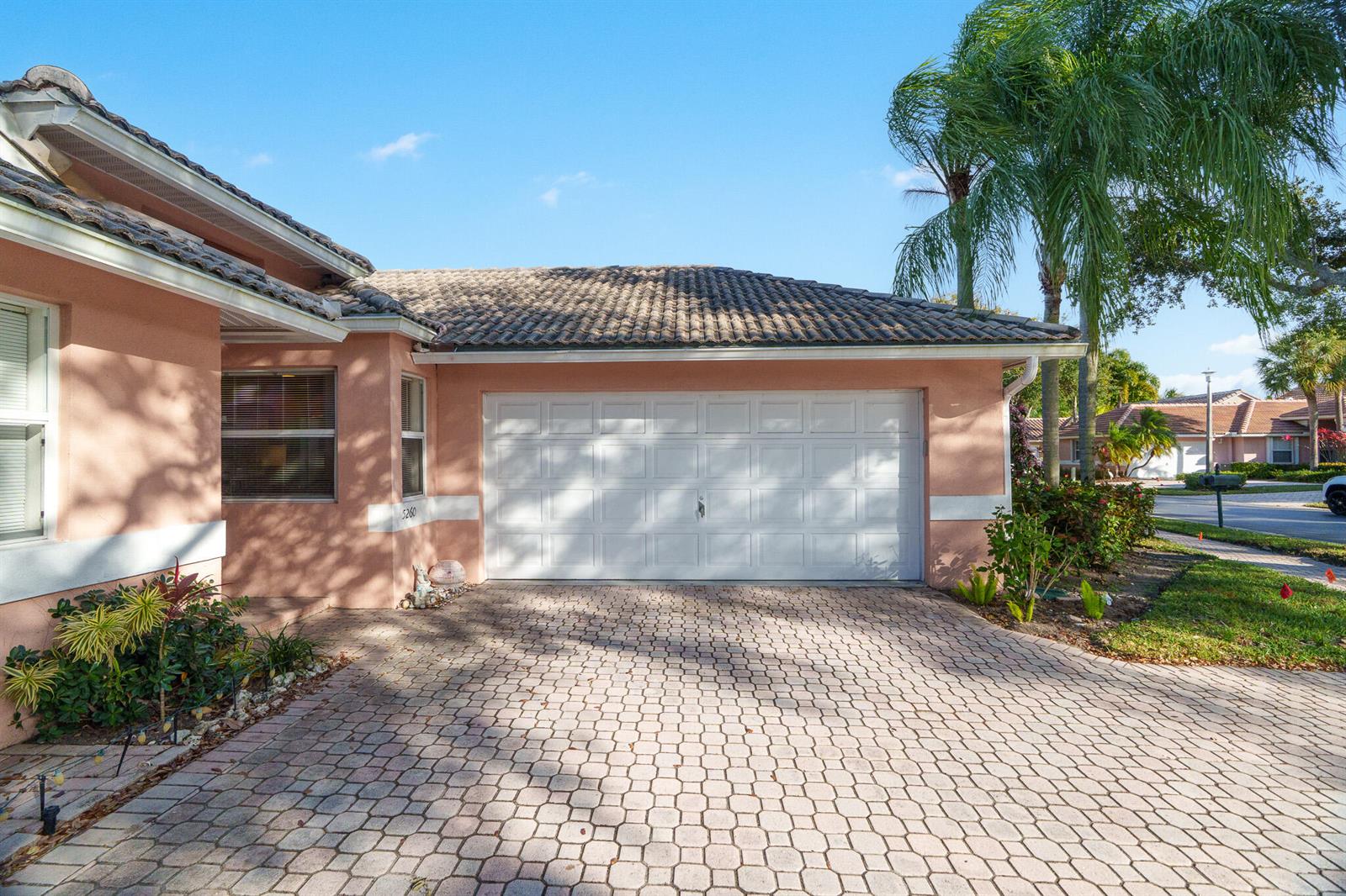 A peach-colored house exterior features a white garage door and a paved driveway — 5260 Grande Palm Circle, Delray Beach FL 33484, DELRAY BEACH, FL