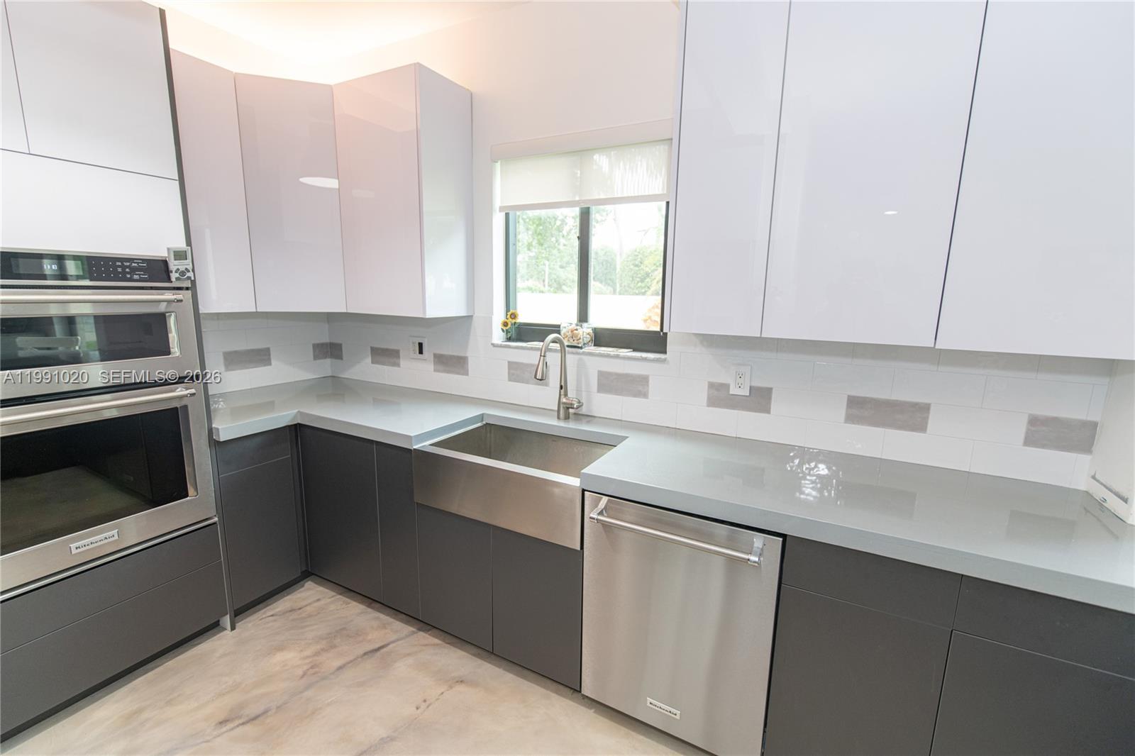 A modern kitchen features gray lower cabinets, white upper cabinets, stainless steel appliances, and countertops — 8694 Via Reale # 3, Boca Raton FL 33496, BOCA RATON, FL