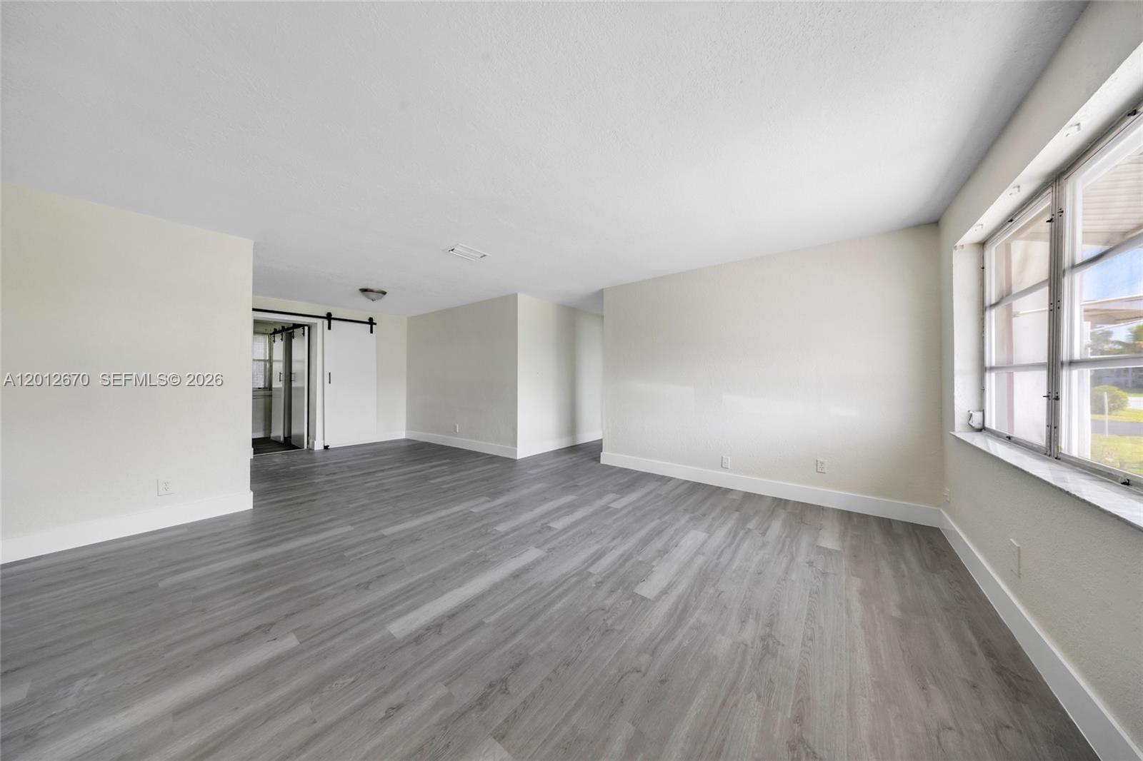 An empty room features light-colored walls, gray wood-look flooring, and a sliding barn door — 2520 NW 2nd Dr, Pompano Beach FL 33064, POMPANO BEACH, FL