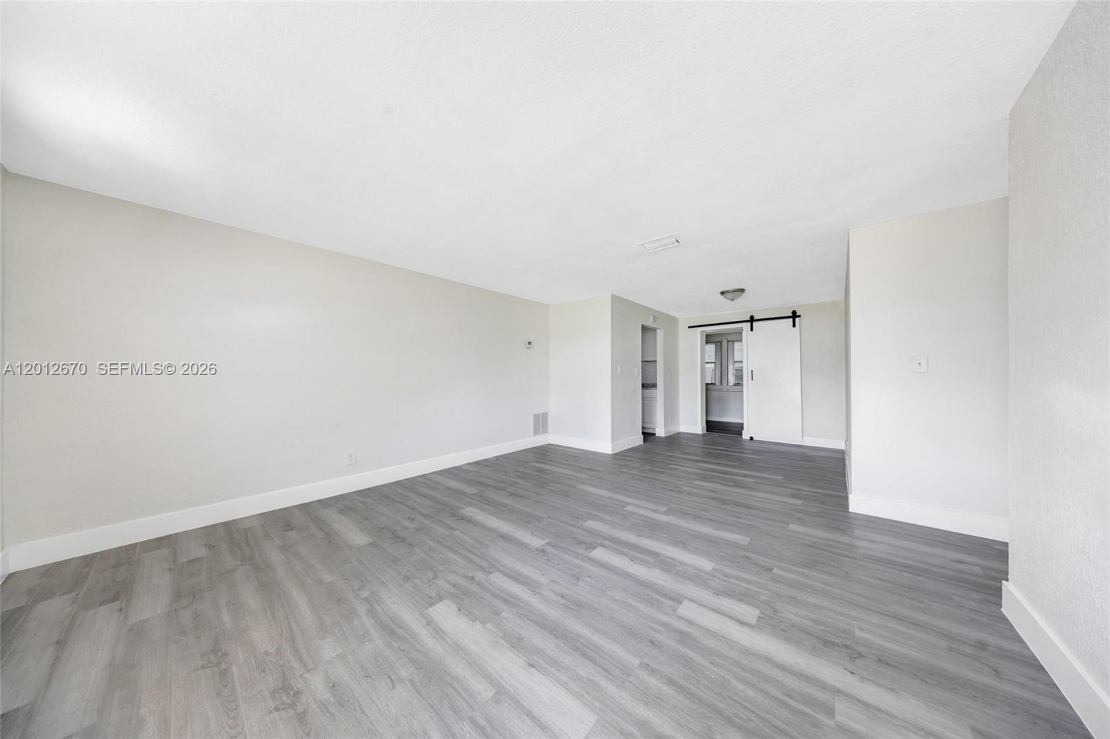 An empty room features gray wood-look flooring, white walls, and a white sliding barn door — 2520 NW 2nd Dr, Pompano Beach FL 33064, POMPANO BEACH, FL