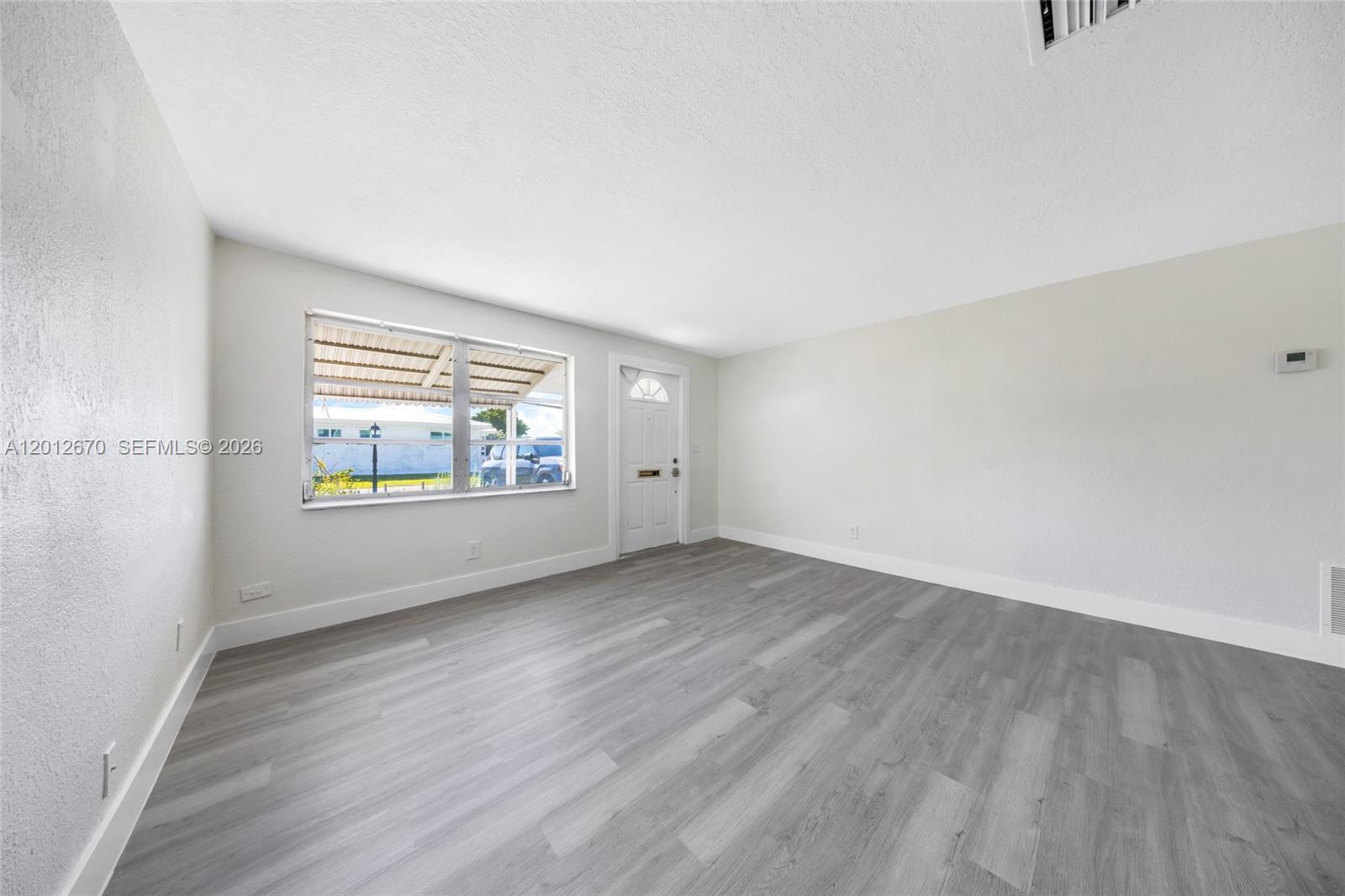 An empty room features light gray wood-look flooring, white walls, a window, and a door — 2520 NW 2nd Dr, Pompano Beach FL 33064, POMPANO BEACH, FL