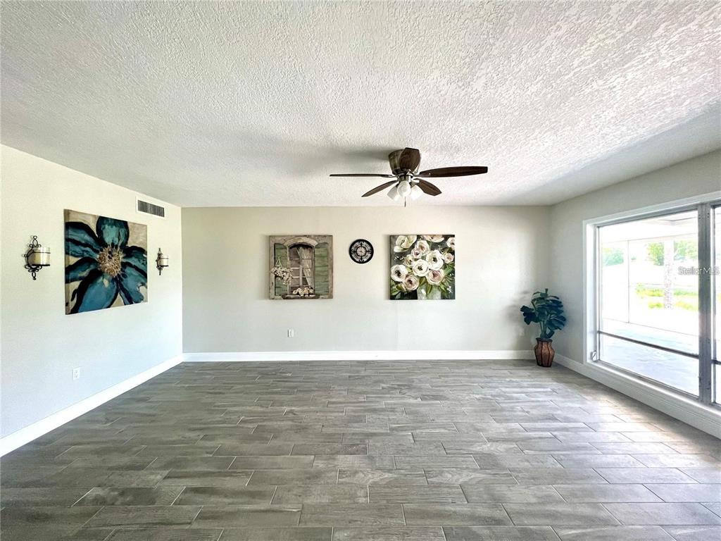 A living room features gray tile flooring, a ceiling fan, and wall art — 912 LA JOLLA AVENUE, SUN CITY CENTER, FL