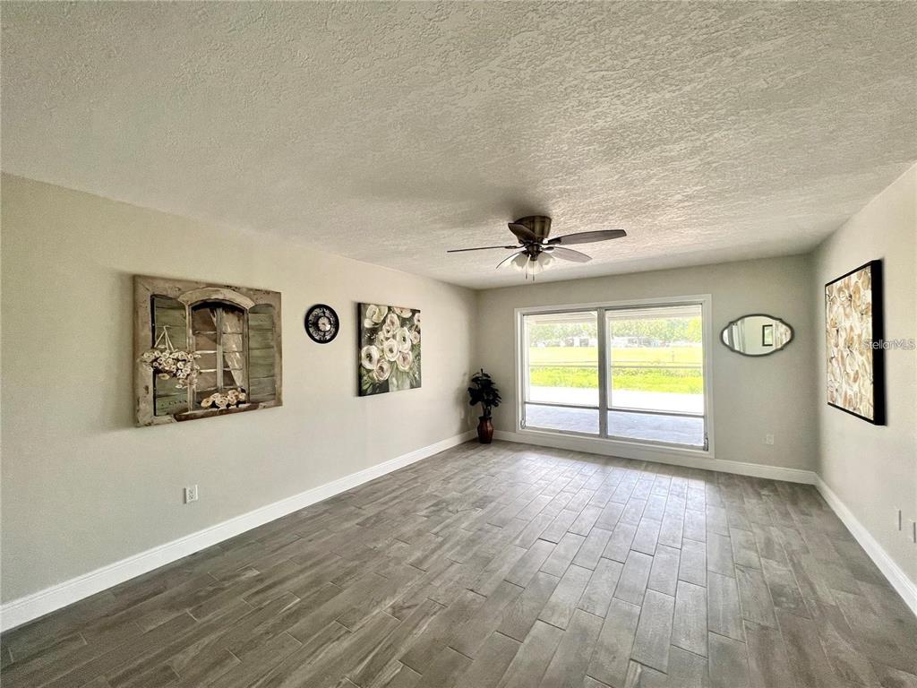 A living room with gray wood-look tile flooring, a ceiling fan, and wall art — 912 LA JOLLA AVENUE, SUN CITY CENTER, FL