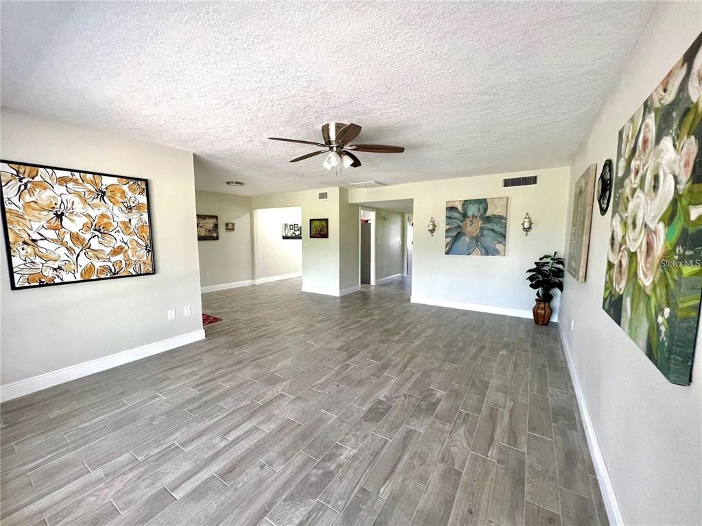 A spacious living room features light gray wood-look tile flooring and several large floral paintings — 912 LA JOLLA AVENUE, SUN CITY CENTER, FL
