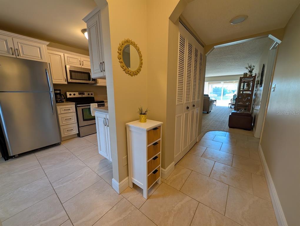 A kitchen with stainless steel appliances and tile flooring opens into a carpeted living area — 802 CORDOVA GREEN UNIT 802, SEMINOLE, FL