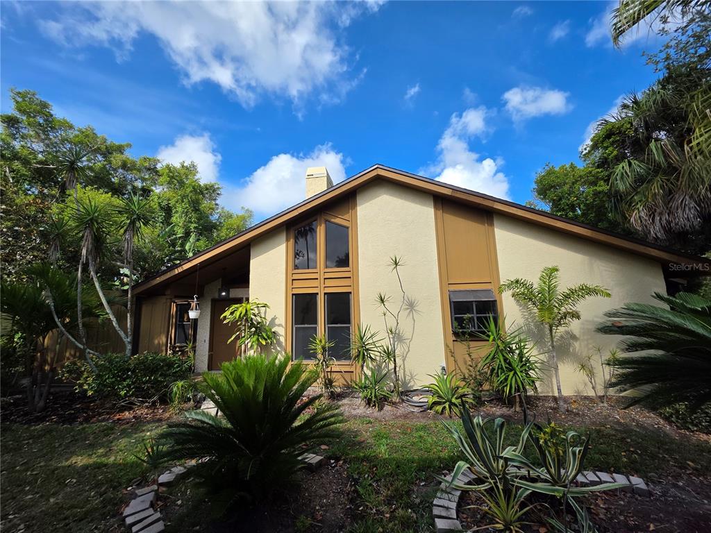 A tan house with brown trim and large windows is surrounded by lush tropical landscaping — 7518 4TH AVENUE W, BRADENTON, FL