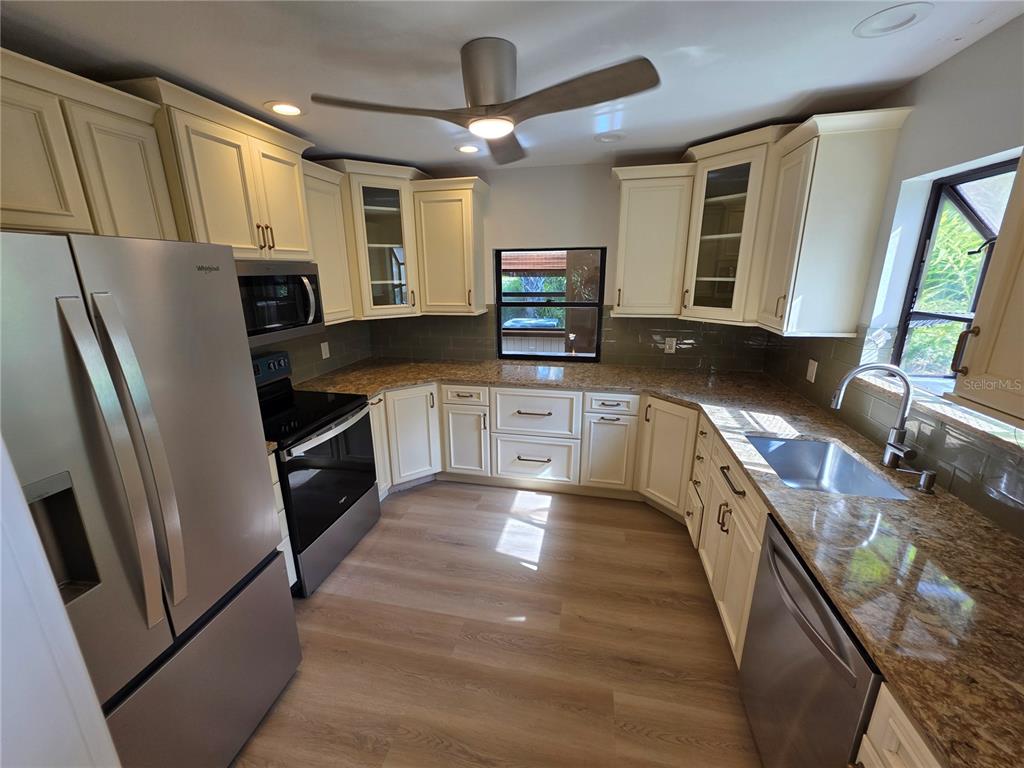 A kitchen features cream-colored cabinets, granite countertops, stainless steel appliances, and light wood-look flooring — 7518 4TH AVENUE W, BRADENTON, FL