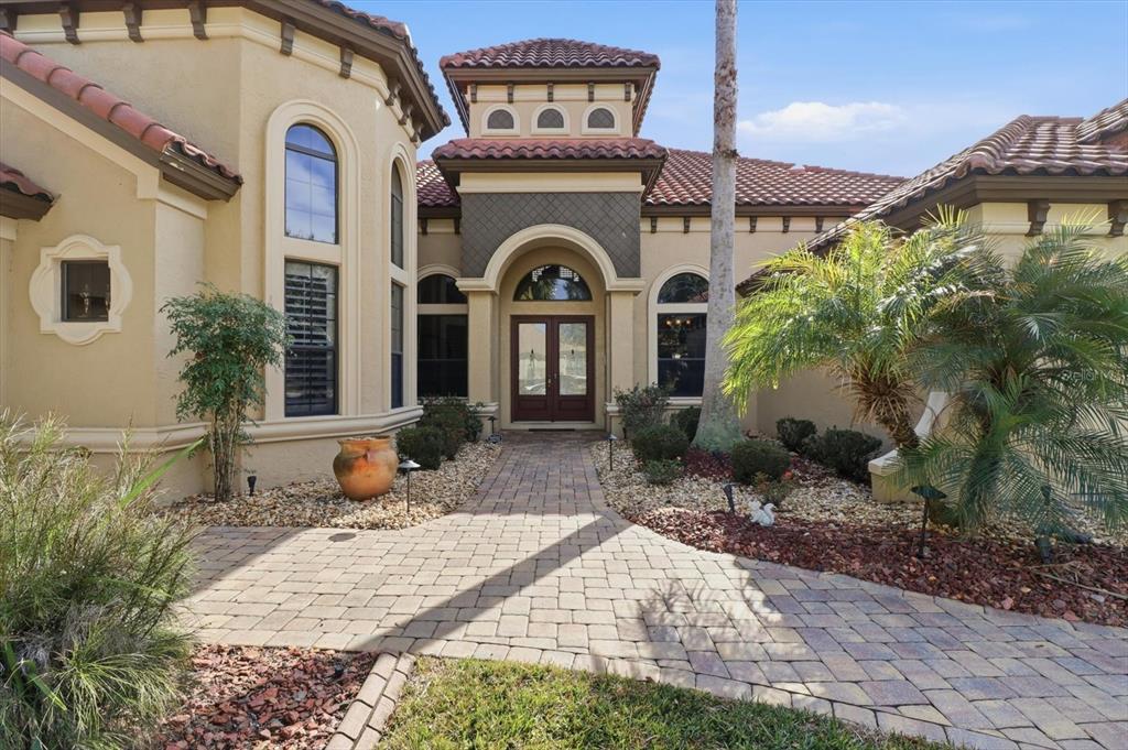A paved walkway leads to the arched front entrance of a Mediterranean-style home with tile roofs — 1416 N RIDGE MEADOW PATH, HERNANDO, FL
