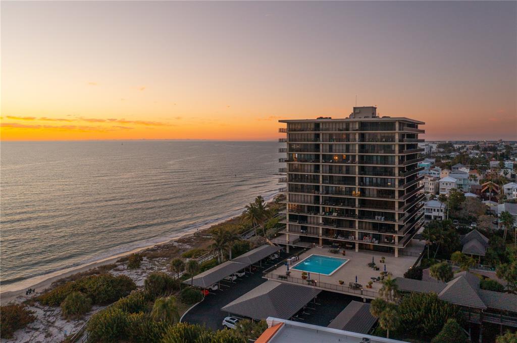 An aerial view of a high-rise condominium building next to a beach at sunset — 7650 BAYSHORE DRIVE UNIT 401, TREASURE ISLAND, FL