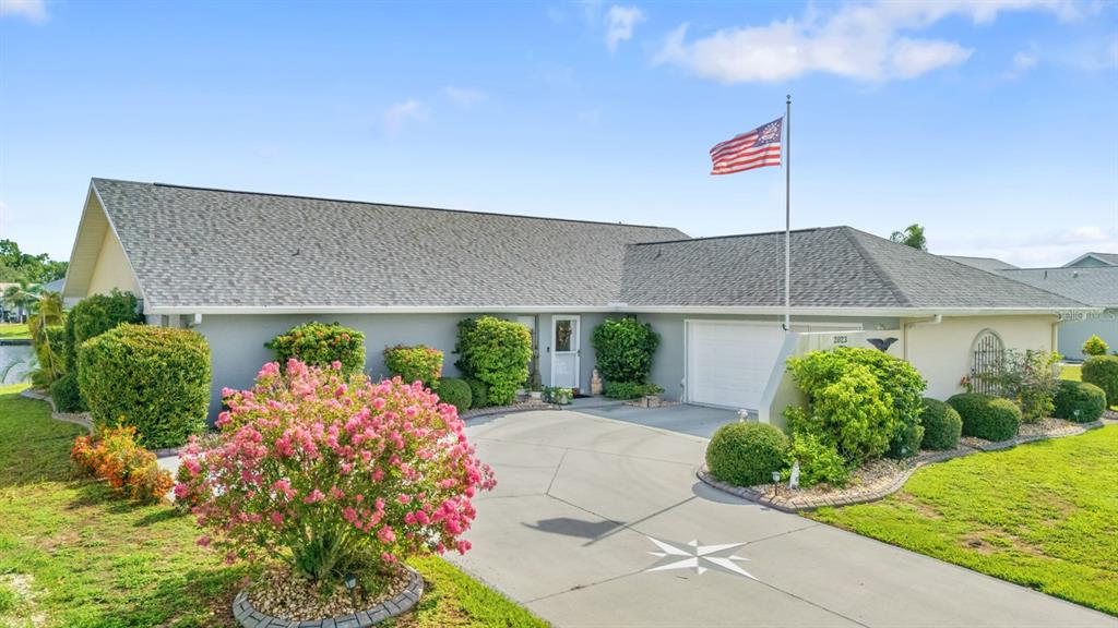 A single-story house with a gray roof, a concrete driveway, and a prominent American flag — 2023 EL RANCHO DRIVE, SUN CITY CENTER, FL