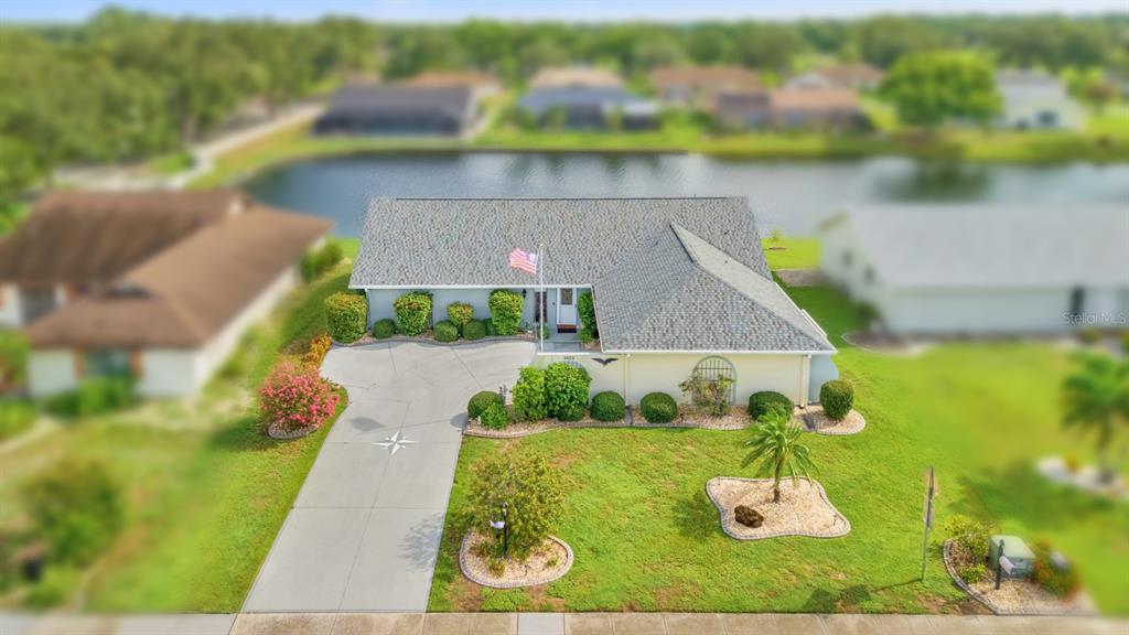 An aerial view of a single-story house with a gray roof, driveway, and backyard pond — 2023 EL RANCHO DRIVE, SUN CITY CENTER, FL
