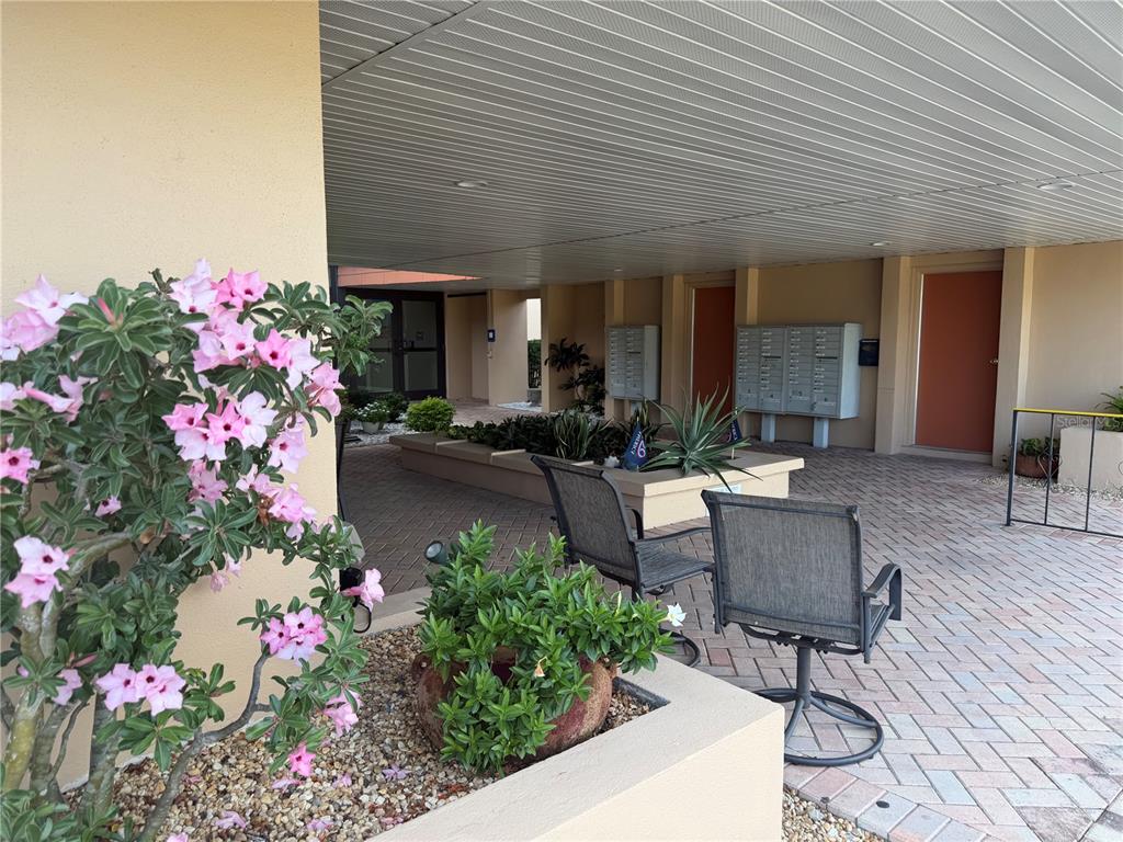 A covered outdoor patio features brick pavers, potted plants, mailboxes, and two chairs — 2290 AARON STREET UNIT 101, PORT CHARLOTTE, FL